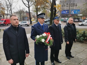 delegacja, w której uczestniczy policjant. Mężczyzna z mundurze galowym trzyma bukiet kwiatów