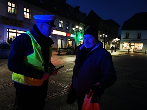 na zdjęciu widać policjanta, który rozmawia z przechodniem. Jest zmrok.