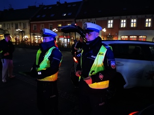 na zdjęciu widać dwóch policjantów drogówki. Mają założone odblaskowe kamizelki. Jest ciemno.