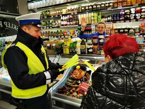 na zdjęciu widać policjanta drogówki, który przekazuje odblaski sprzedawczyniom sklepu