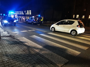 na zdjęciu widać przejściu dla pieszych, na którym stoi biały samochód, w tle policyjny radiowóz oraz policjanci