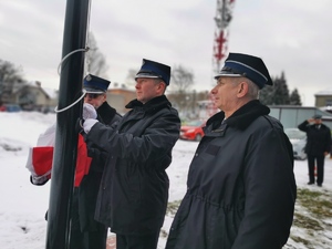 na zdjęciu widać trzech strażaków ochotników wprowadzających flagę na maszt