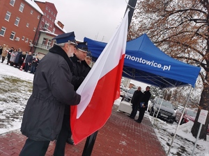 na zdjęciu widać trzech strażaków ochotników wprowadzających flagę na maszt