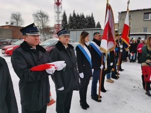 na zdjęciu widać stojących w rzędzie uczestników uroczystości, w tym strażaków ochotników, którzy trzymają złożoną jeszcze flagę