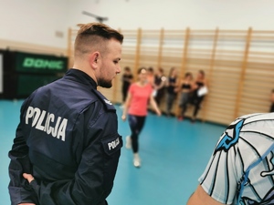 na zdjęciu widać policjanta w mundurze, w tle uczestniczki kursu w strojach sportowych