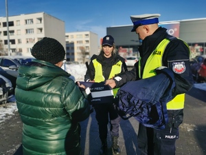 na zdjęciu policjantów w odblaskowych kamizelkach, którzy rozdawają seniorom odblaski