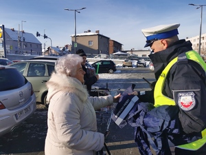 na zdjęciu policjant wręcza odblask starszej kobiecie. Mundurowy ma na sobie odblaskową kamizelkę