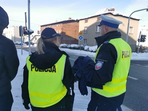 na zdjęciu widać dwoje policjantów w odblaskowych kamizelkach. Mundurowi stoją na chodniku w centrum miasta