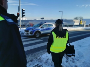 na zdjęciu widać policjantów oczekujących na wejście na pasy. W tle policyjny radiowóz