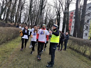 na zdjęciu widać uczestników biegu, którzy szykują się do dalszej trasy. Jeden z nich rozmawia z policjantem drogówki