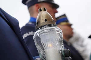 zdjęcie przedstawia zapalony znicz, w tle policjanci