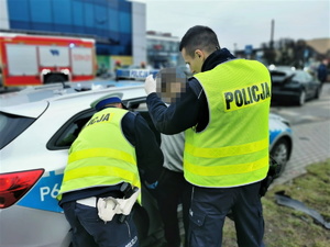 policjanci drogówki stoją przy radiowozie, trzymają mężczyznę