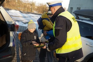 na zdjęciu policjant drogówki przekazuje odblaskową opaskę małemu chłopcu