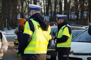 policjanci drogówki ubrani w odblaskowe kamizelki rozdają odblaskowe opaski, scena ma miejsce w centrum Ornontowic