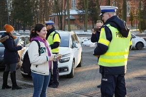 policjanci drogówki ubrani w odblaskowe kamizelki rozdają odblaskowe opaski, scena ma miejsce w centrum Ornontowic