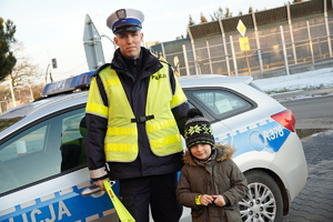 policjant drogówki pozuje do zdjęcia z dzieckiem. Za nimi policyjny radiowóz