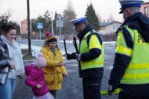 policjanci drogówki w odblaskowych kamizelkach rozdają opaski z logo radia Ekspress