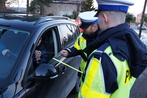 policjanci przekazują odblaskowe opaski kobiecie siedzącej w samochodzie