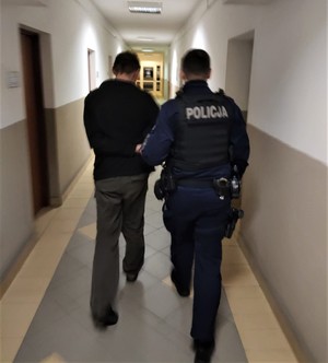 na zdjęciu widać policjanta, który korytarzem prowadzi zatrzymanego mężczyznę