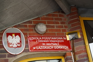 na zdjęciu widać tabliczkę z godłem Polski, obok tablica informacyjna: Szkoła Podstawowa numer 6 w Łaziskach Górnych