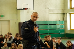 policjant prewencji podczas zajęć z uczniami łaziskiej podstawówki. Mężczyzna trzyma mikrofon