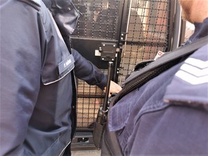 policjanci zamykają kratę pomieszczenia dla zatrzymanych w radiowozie