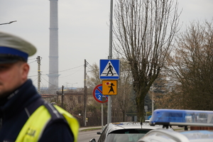 na zdjęciu policjant mikołowskiej drogówki oraz znaki drogowe: pieszy i UWAGA dzieci