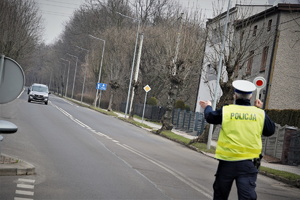 na zdjęciu widać policjanta drogówki na ulicy, który zatrzymuje do kontroli jadący samochód