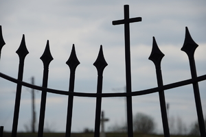 zdjęcie przedstawia fragment ogrodzenia cmentarza. Głównym elementem jest krzyż