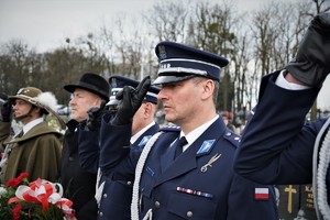 policjanci w mundurach galowych oraz pozostali mundurowi i przedstawiciele samorządu stoją  w rzędzie na cmentarzu w Ornontowicach. Zbliżenie na komendanta Policji