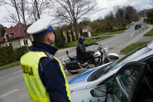 policjant drogówki stoi obok radiowozu, w tle motocyklista