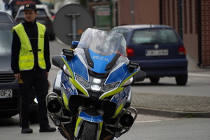 stojący na ulicy policyjny motocykl, za nim stoi strażnik miejski