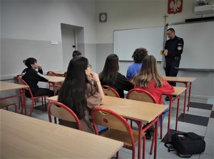 Na zdjęciu widać policjanta, który rozmawia z uczniami. Scena ma miejsce w klasie szkolnej.