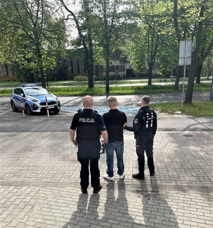 policjanci prowadzą zatrzymanego. W tle policyjny radiowóz