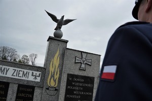 na zdjęciu widać pomnik na cmentarzu, na nim rzeźba ptaka, widać też fragment policyjnego munduru