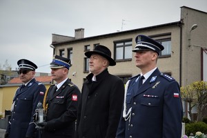 policjanci, strażak oraz starosta stoją przed pomnikiem na cmentarzu parafialnym