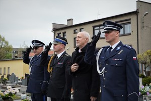 policjanci, strażak oraz starosta stoją przed pomnikiem na cmentarzu parafialnym, mundurowi salutują