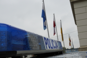 na zdjęciu widać fragment policyjnego radiowozu, w tle flagi na masztach przed bazyliką w Mikołowie