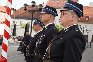 trzech strażaków przy maszcie z flagą