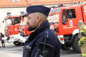 policjant prewencji w mundurze ćwiczebnym w tle wozy strażackie