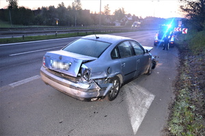 stojący na pasie drogi krajowej samochód z uszkodzoną karoserią, za nim stoją policjanci