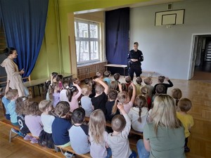 sala w budynku przedszkola, dzieci siedzą na materacach, przed nimi stoi policjantka i omawia temat bezpieczeństwa