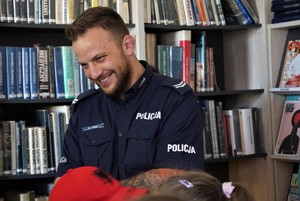 policjant w bibliotece. Za nim stoi regał z książkami