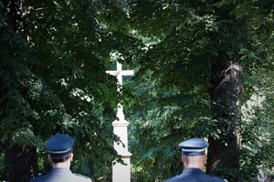 dwaj umundurowani policjanci na terenie cmentarza, w tle krzyż