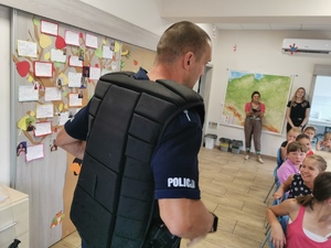 policjant prezentuje dzieciom policyjną kamizelkę odblaskową