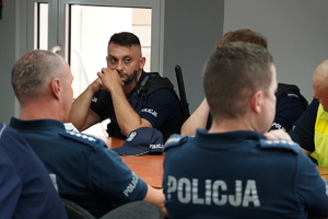 zdjęcie przedstawia siedzącego przy stole policjanta prewencji podczas odprawy