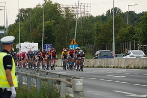 po lewej stoi policjant drogówki, po prawej peleton Tour de Pologne