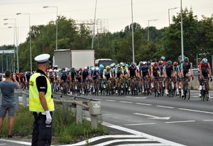 po lewej stoi policjant drogówki, po prawej peleton Tour de Pologne