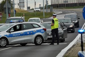 stojący na drodze radiowóz, obok niego policjant, za nim samochody