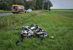 leżący w rowie rozbity motocykl, w oddali na jezdni stoi karetka